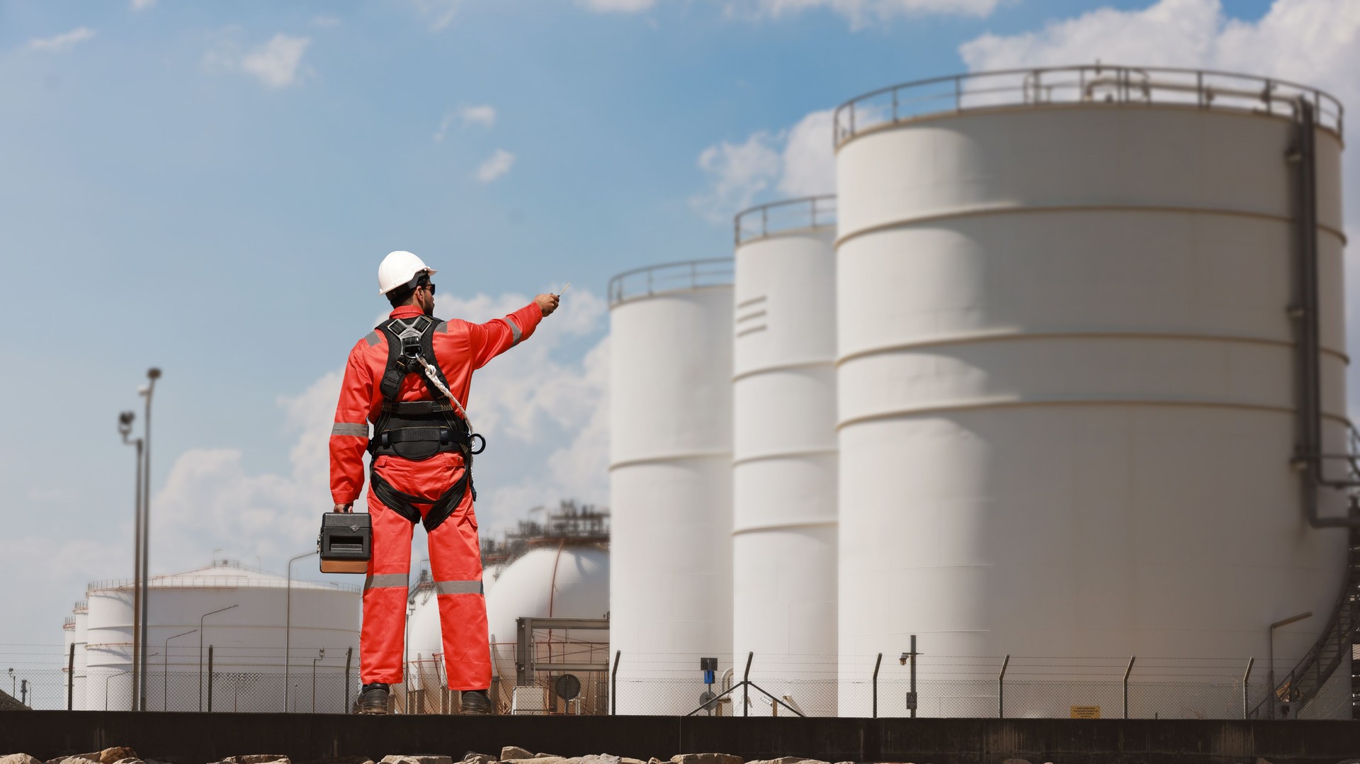 Construction foreman wearing safety harness and  orange safety uniform standing in front of petrochemical storage